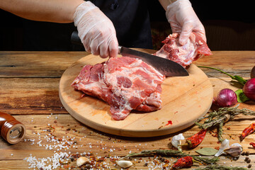 The chef uses his hands to slice pork ribs with a knife on a wooden cutting table. Selective focus. The concept of the cooking process.