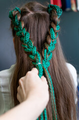 Back view of a teenage girl with dark long hair and a hairstyle from colored braids indoors