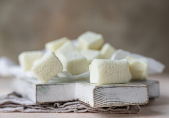 Yellow square shape marshmallow on wooden cutting board, light concrete background. Close up.