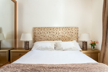 Clean and simplistic looking beige colored bedroom, in it, a white bed with pillows and a nightstand on each side. Real estate.