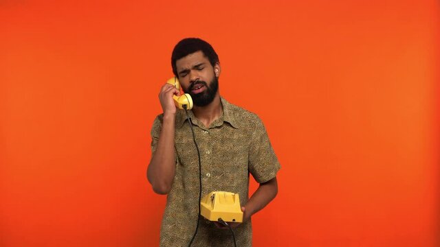 displeased african american man talking on retro telephone isolated on orange