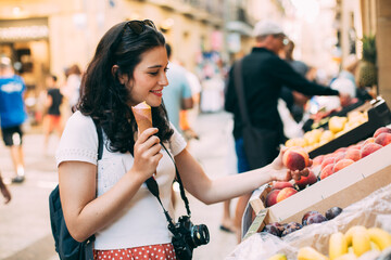 Young tourist woman eating an ice cream and buying some fruit in a street market