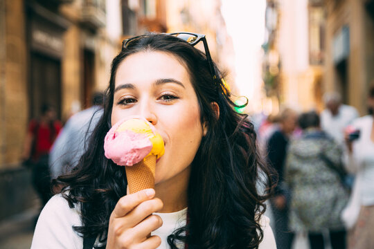 Happy young beautiful woman eating a big ice cream in the street