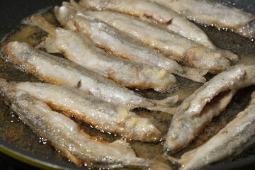 Fried fish in a frying pan. Small crispy fish are fried in oil. Shallow depth of field