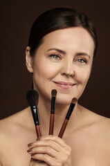 Beautiful middle aged woman with a makeup brushes on brown background