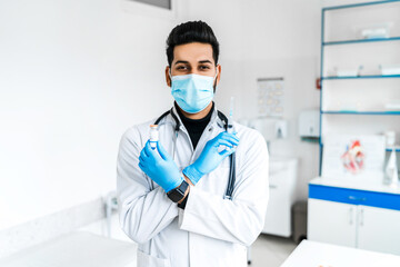 A male doctor in a protective mask and gloves holds an ampoule and injections for vaccination, in the middle of a modern hospital. Safe vaccination