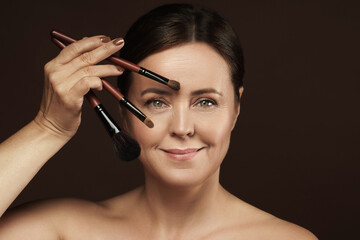 Beautiful middle aged woman with a makeup brushes on brown background