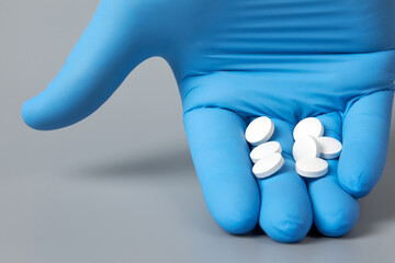 Fototapeta premium A blue-gloved hand holds the pills against a gray background. The doctor delivers the pills