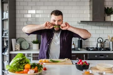 Handsome Man eating Green Onion and having fun cooking fresh healthy food with organic vegetables at home in modern kitchen, copy space, food commercial