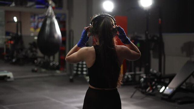 Fit female boxer walks by boxing gym in headphones, warming up