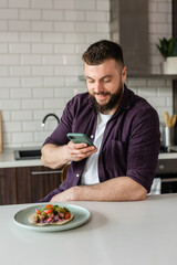 Man taking photos with food using a smartphone at home in modern kitchen sitting at table ready to eat tasty meal with Mexican food on Daylight, Portrait 