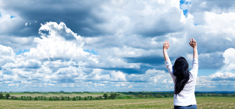 Young girl with raised arms. Against a background of blue sky and clouds. Joy. Prayer and worship to God.