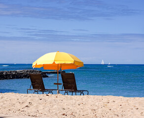 Yellow beach umbrella with deck chairs on sandy beach with blue sea and sky.
