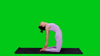 Young sporty slim woman in bodysuit practicing yoga camel pose on mat against green screen background