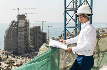 Architect or businessman wearing hard hat with a bluepritns on a construction site near blue sea