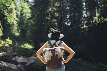 Stylish woman traveler relaxing on at waterfall in mountains, back view. Travel and wanderlust