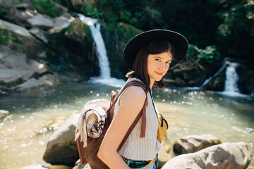 Stylish woman traveler relaxing on background of waterfall in mountains. Travel and wanderlust