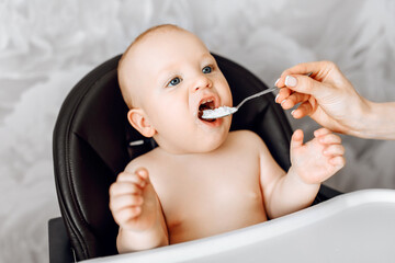 Mom feeds baby from a spoon, the baby sits in a highchair