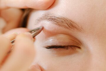 Young woman smooths her eyebrows with tweezers. Shallow depth of field