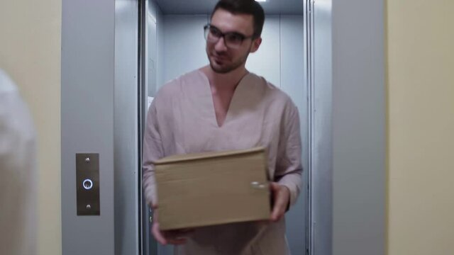 Young couple of two men holds cardboard boxes and etting out of the elevator, moving in to new appartment