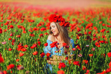 Naklejka na ściany i meble Beautiful young woman walks in a field with poppy flowers at sunset.