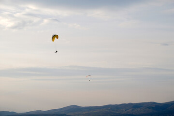 Paraglider flying in the sky over the mountain landscape.