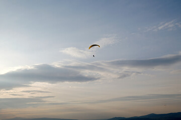 Paraglider flying in the sky over the mountain landscape.