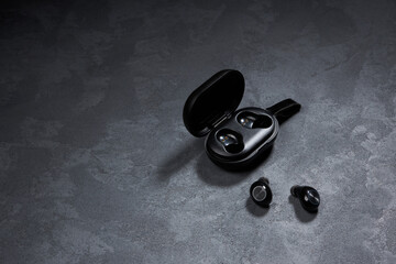 Naklejka na ściany i meble Wireless earphones with charger case on a dark background. Black headphones for smarphone, headset closeup 