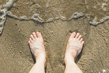 Asian Caucasian male feet on the sand with a wave comes in, on holiday. copy space.top view.