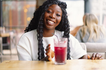 African woman with afro hair is drinking a cocktail.