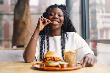 African woman with afro hair eating a tasty classic burger with fries.
