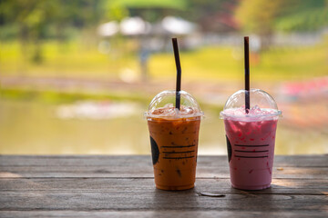 Iced pink milk  with iced tea in plastic cup with straw on wood table on nature background