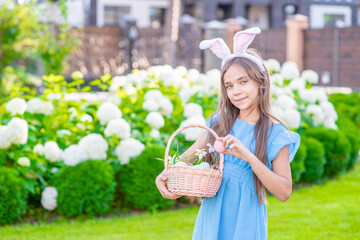 Smiling young girl wearing Easter bunny ears holds basket of a Easter eggs. Empty space for text