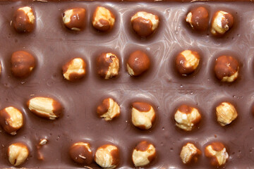 close-up of milk chocolate bar with whole hazelnuts. selective focus. top view