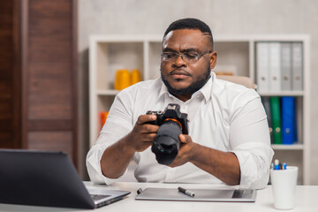 Freelance photographer workplace at home office. Young African-American man works using a computer, graphics tablet and other devices. Remote job.