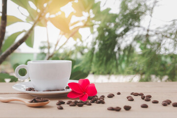 A white hot coffee cup with a saucer and spoon is placed on a wooden plate on the landscape nature background.