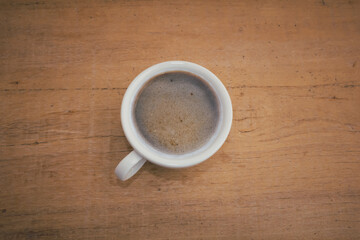 A hot coffee cup and milk froth are on a wooden background.