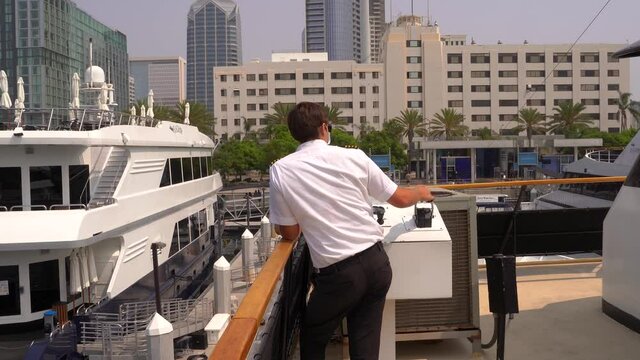 Ship captain master in uniform docking the vessel into its dock in the city of San Diego, California on a sunny day