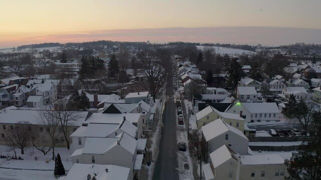 Descending aerial on small old town in United States. Winter snow covers rooftops as sunrise, sunset. Establishing, pedestal shot in USA.