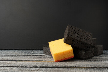 kitchen sponges on a black background with copy space. one yellow dishwashing sponge among many black ones.
