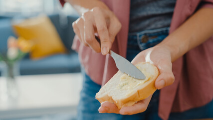 Hands of young Asian woman chef spreading butter on rustic rye bread with metal knife on wooden board on kitchen table in house. Fresh homemade bread production, Healthy eating and traditional bakery.