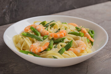 Close up Tagliatelle pasta with shrimps and green beans in white dish with grated Parmesan cheese. Mediterranean cuisine. Italian food.