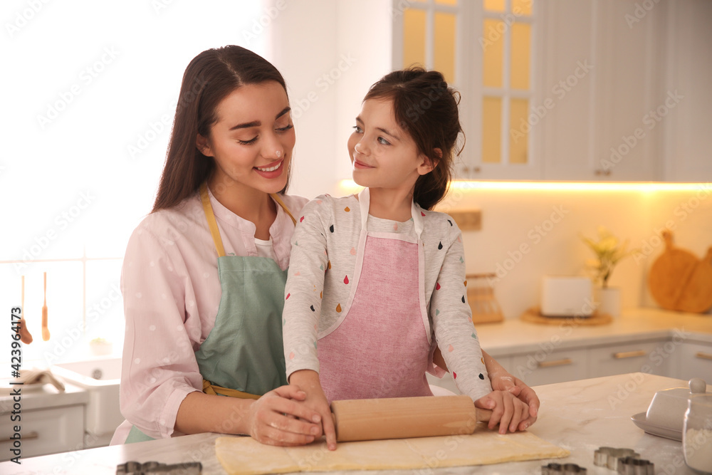 Wall mural Mother with her cute little daughter rolling dough in kitchen