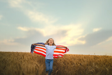 Adorable patriotic girl wearing an American flag in a beautiful wheat field
