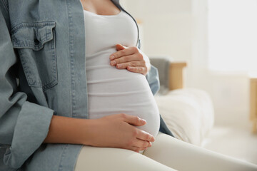 Pregnant woman touching her belly indoors, closeup