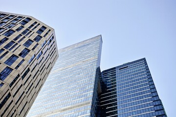 Modern office buildings against bright blue sky. Bottom-up view. Glass facades of skyscrapers with contrasting highlights and reflections. Economy development, finance and business concept. Downtown.