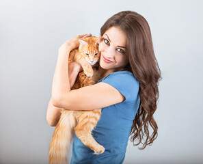 Happy young woman holding on the hands her red maine coon kitten and hugging with love. Closeup portrait