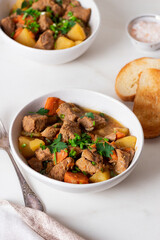 Goulash, beef stew with vegetables and thyme in a white plate with onion and greens.