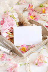 Blank card on a wooden tray between pink flowers