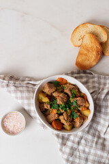 Goulash, beef stew with vegetables and thyme in a white plate with onion and greens.